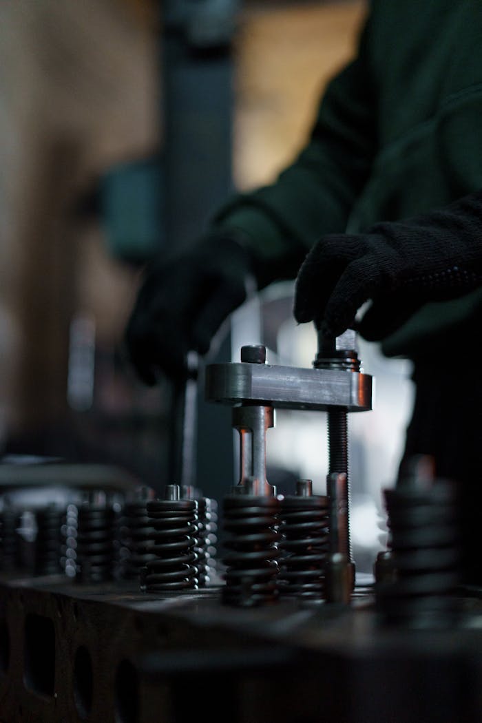 Mechanic adjusting valve springs in dimly lit workshop setting.